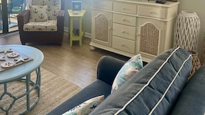 Een woonkamer met een bank, een kleine ronde tafel, een televisie en een kast. Er is een raam met uitzicht op groen.