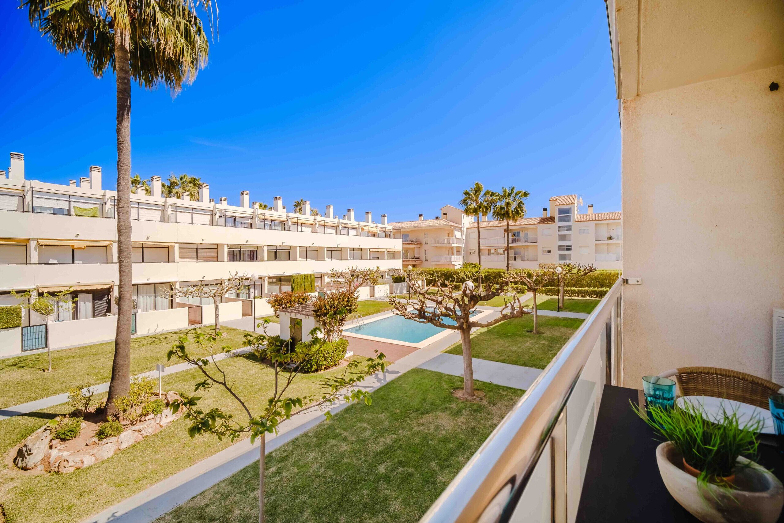 A balcony with a view of a courtyard featuring a swimming pool, palm trees, and a row of buildings.