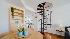 A modern kitchen with white cabinets, a black spiral staircase, and a dining area with a wooden table and chairs. - Santa Barbara Serena Apartment Jávea (Javea / Xàbia)