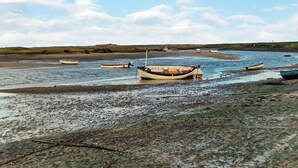 Eine Küstenlandschaft mit mehreren Booten, die in flachem Wasser vor Anker liegen, umgeben von einem Kiesstrand und grasbewachsenen Dünen.