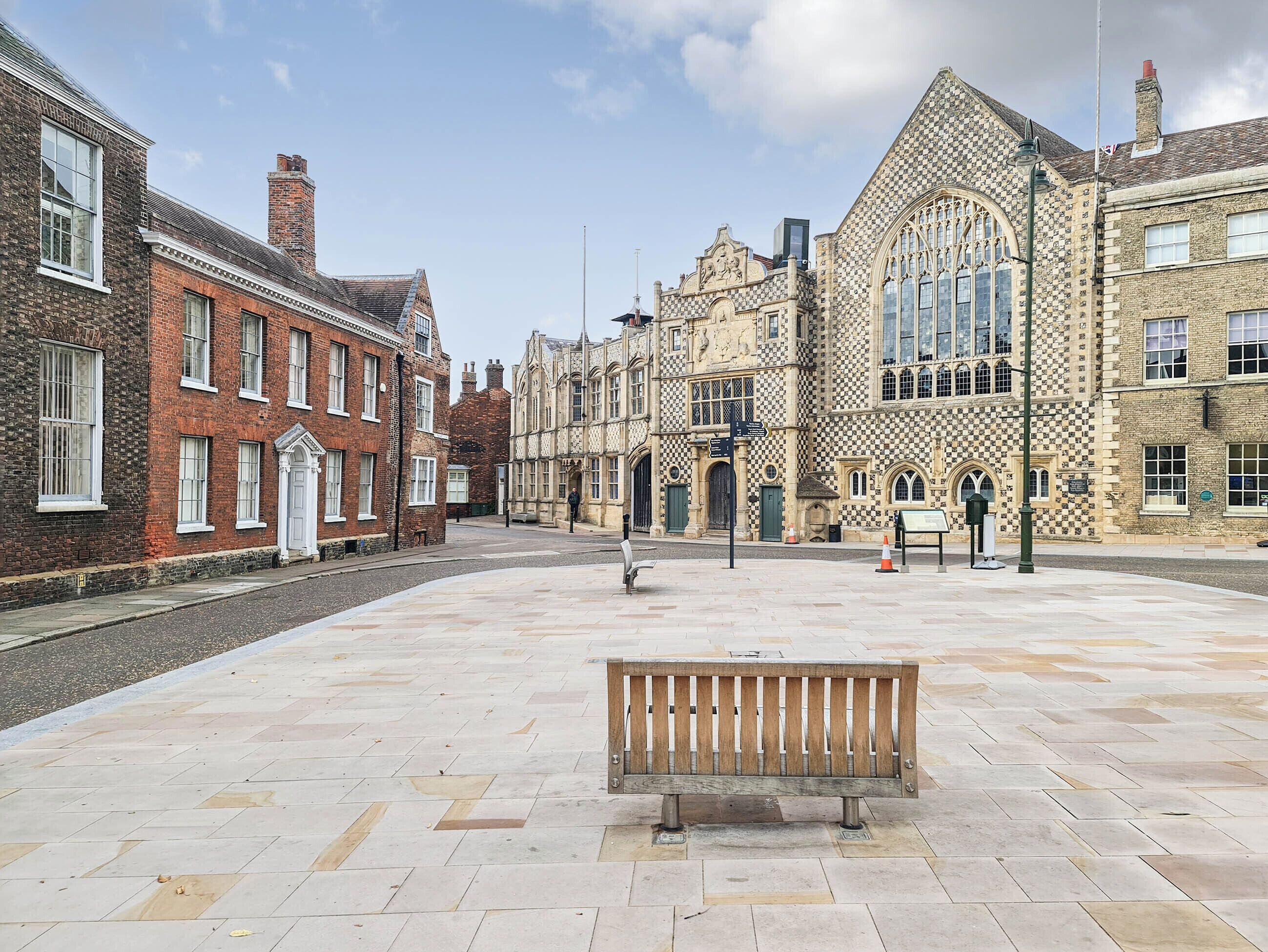 A spacious public square with a wooden bench in the center, surrounded by historic buildings with varied architectural styles.