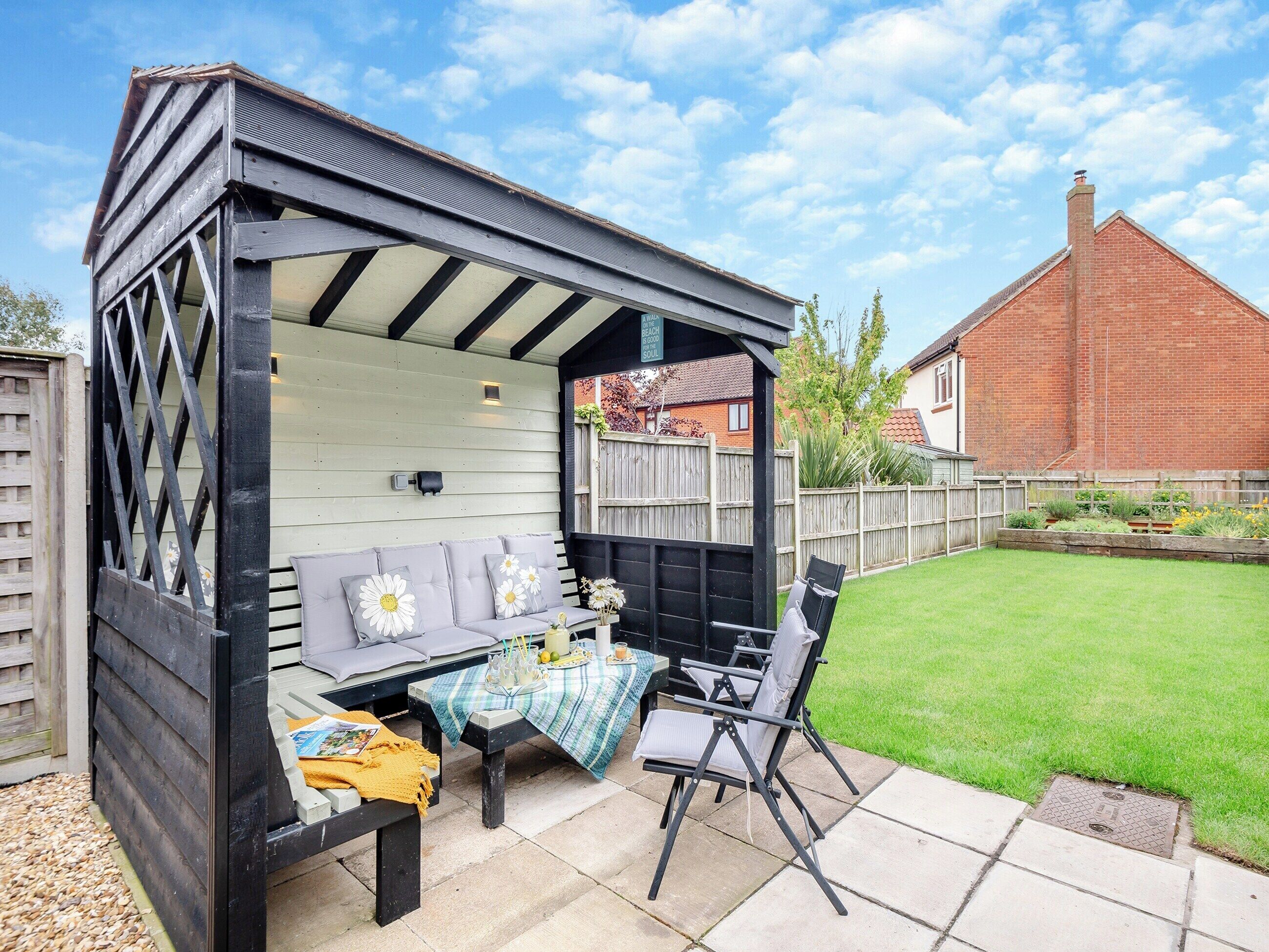 A covered outdoor seating area with a table and chairs, a bench, and a garden view.