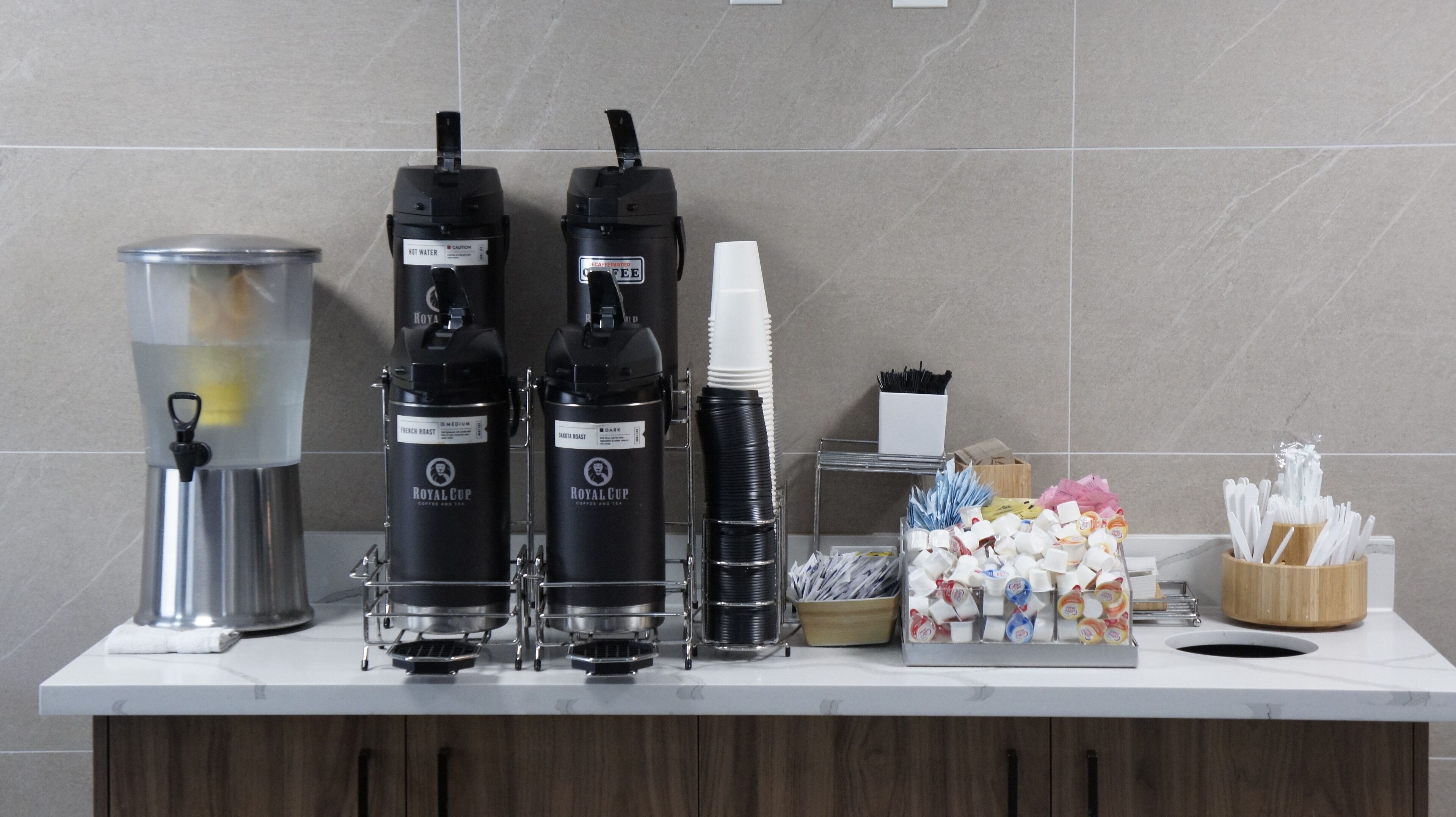 A coffee station with two Royal Cup coffee machines, a water dispenser, and a variety of disposable cups and utensils.
