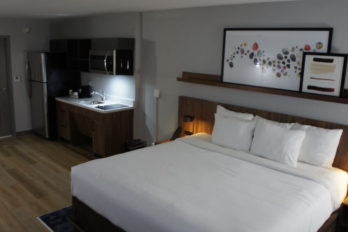 A hotel room with a bed, a small kitchenette, and a framed artwork above the bed.