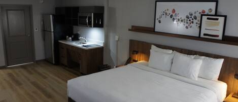 Habitación de hotel con cama, kitchenette pequeño y una obra de arte enmarcada sobre la cama.