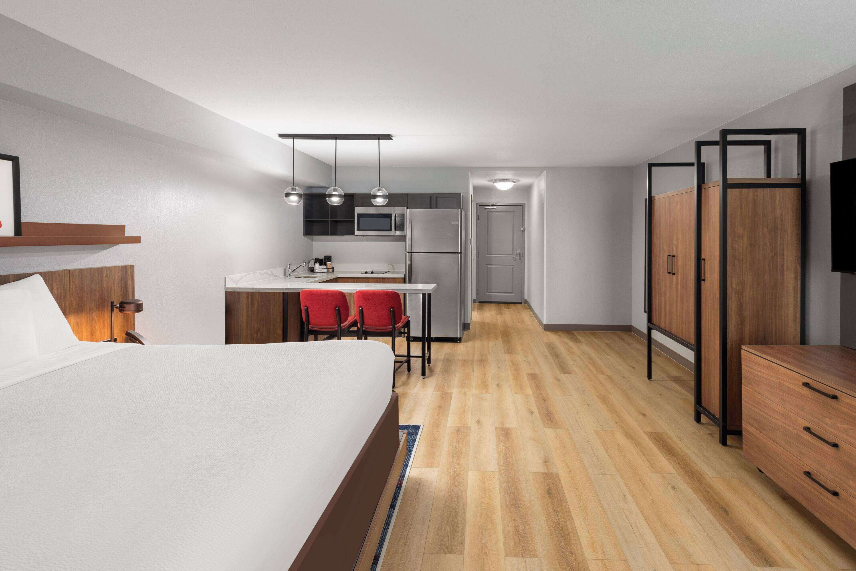Une chambre d’hôtel de taille réduite comprenant un lit, une petite kitchenette, un bureau avec deux chaises et une armoire.