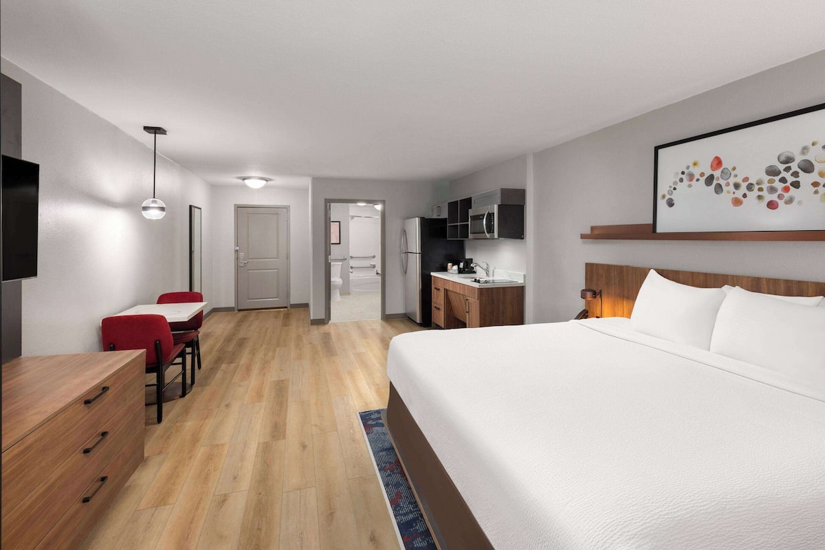 A hotel room with a large bed, a desk, a chair, a TV, and a microwave.