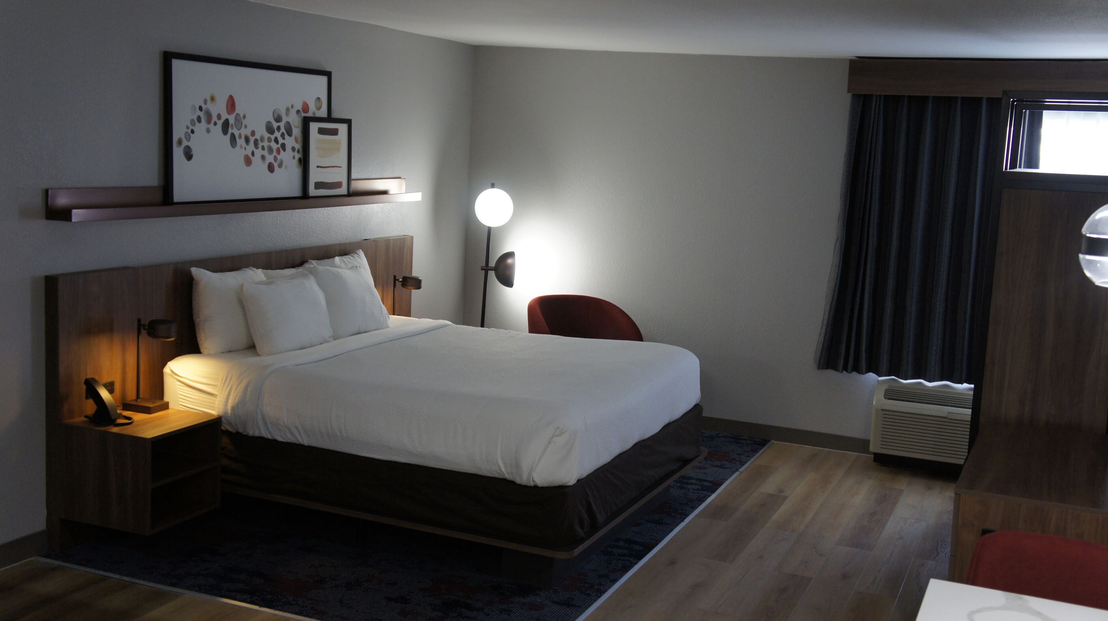 Una habitación de hotel con cama, mesita de noche, lámpara y una obra de arte enmarcada en la pared.