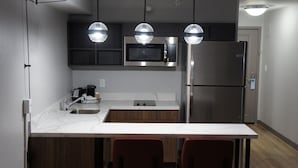 Cozinha moderna com micro-ondas embutido, geladeira de aço inoxidável e bancada branca.