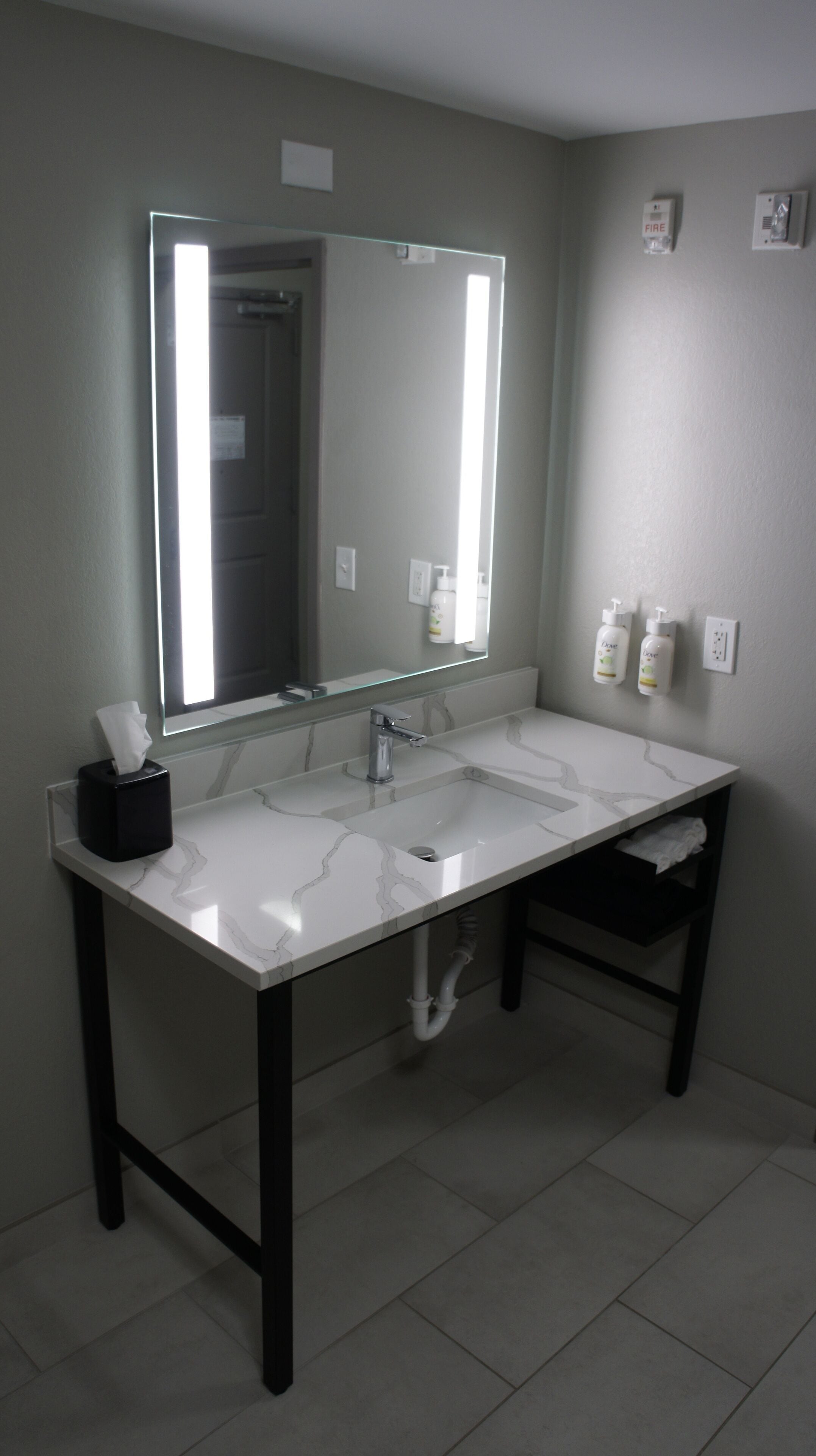 Un baño con un lavamanos blanco, un espejo y dos secamanos.