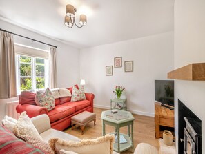 Un salon avec un canapé rouge, une table basse en verre et un téléviseur. Il y a une fenêtre avec des rideaux et une cheminée.