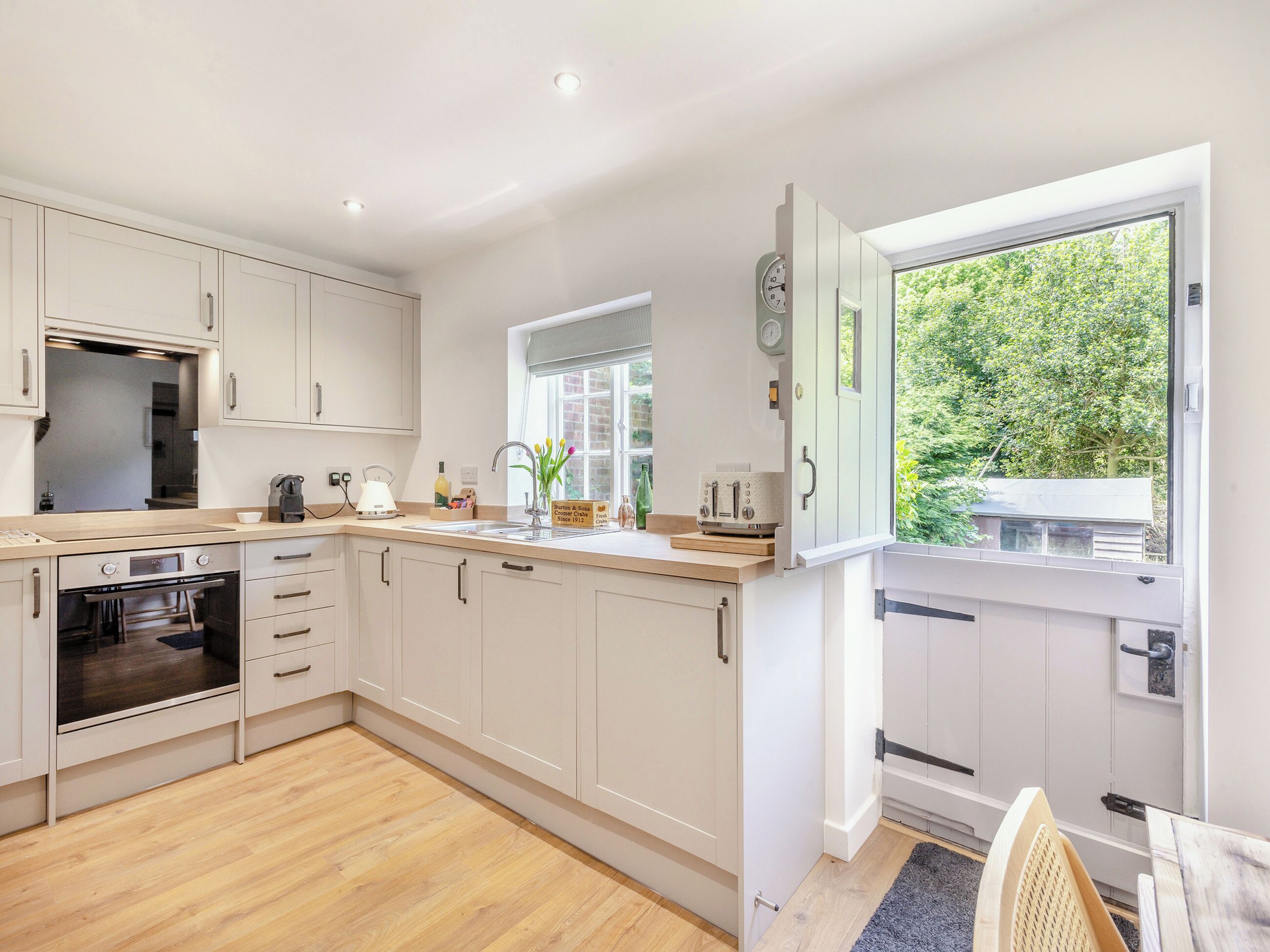 A modern kitchen with white cabinets, a built-in oven, and a window with a view of greenery.