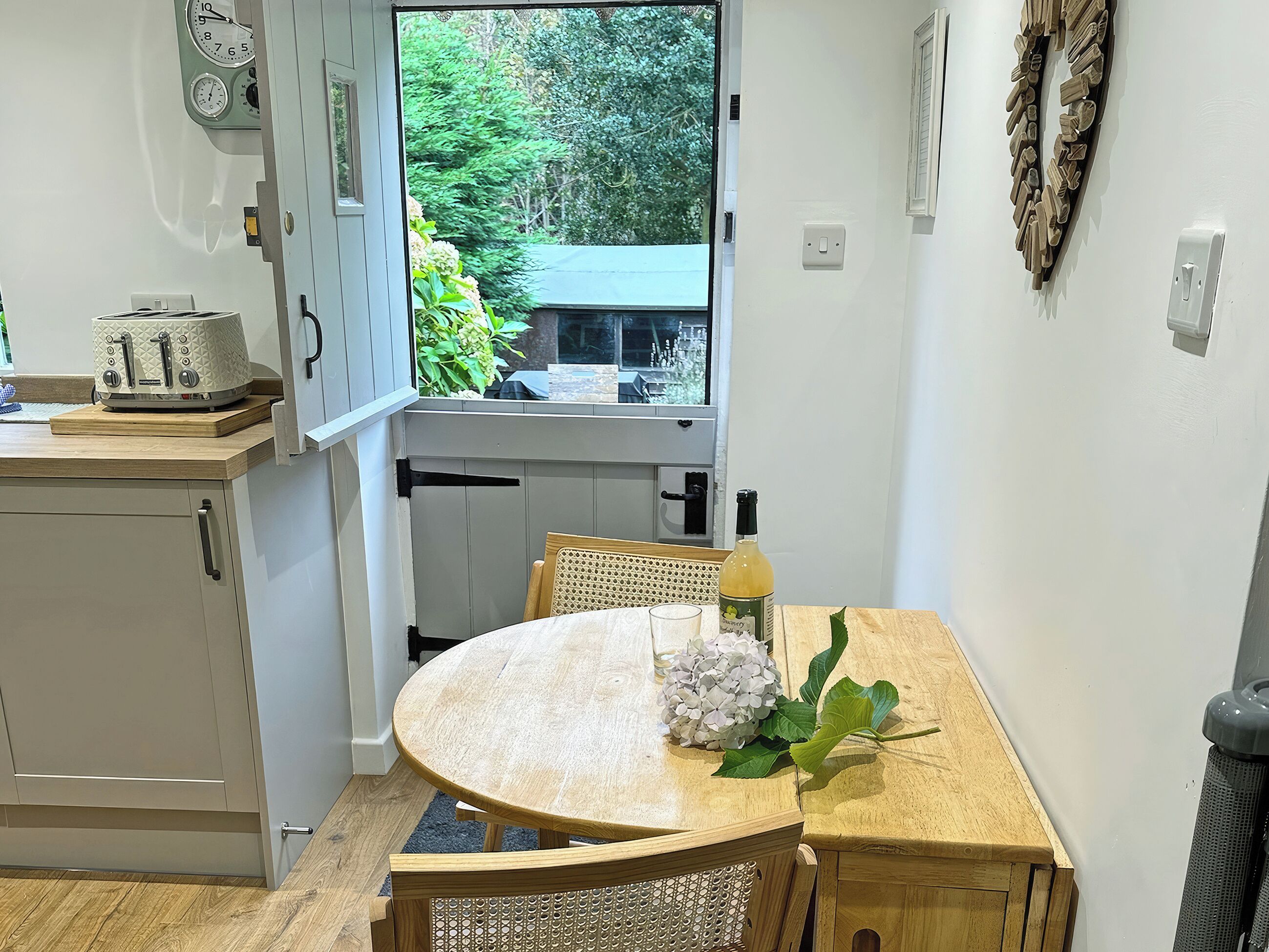 A compact kitchen with a dining table, chairs, a toaster, and a window with a view of greenery.