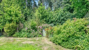 A lush garden with a variety of trees and shrubs, a wooden fence, and a grassy area. - 2 bedroom accommodation in Cromer (Cromer)