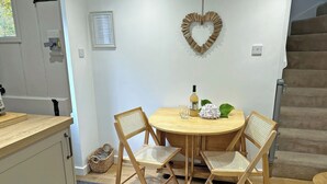 A dining area with a round wooden table, four wicker chairs, a heart-shaped decoration, a bottle, and a glass on the table. - 2 bedroom accommodation in Cromer (Cromer)