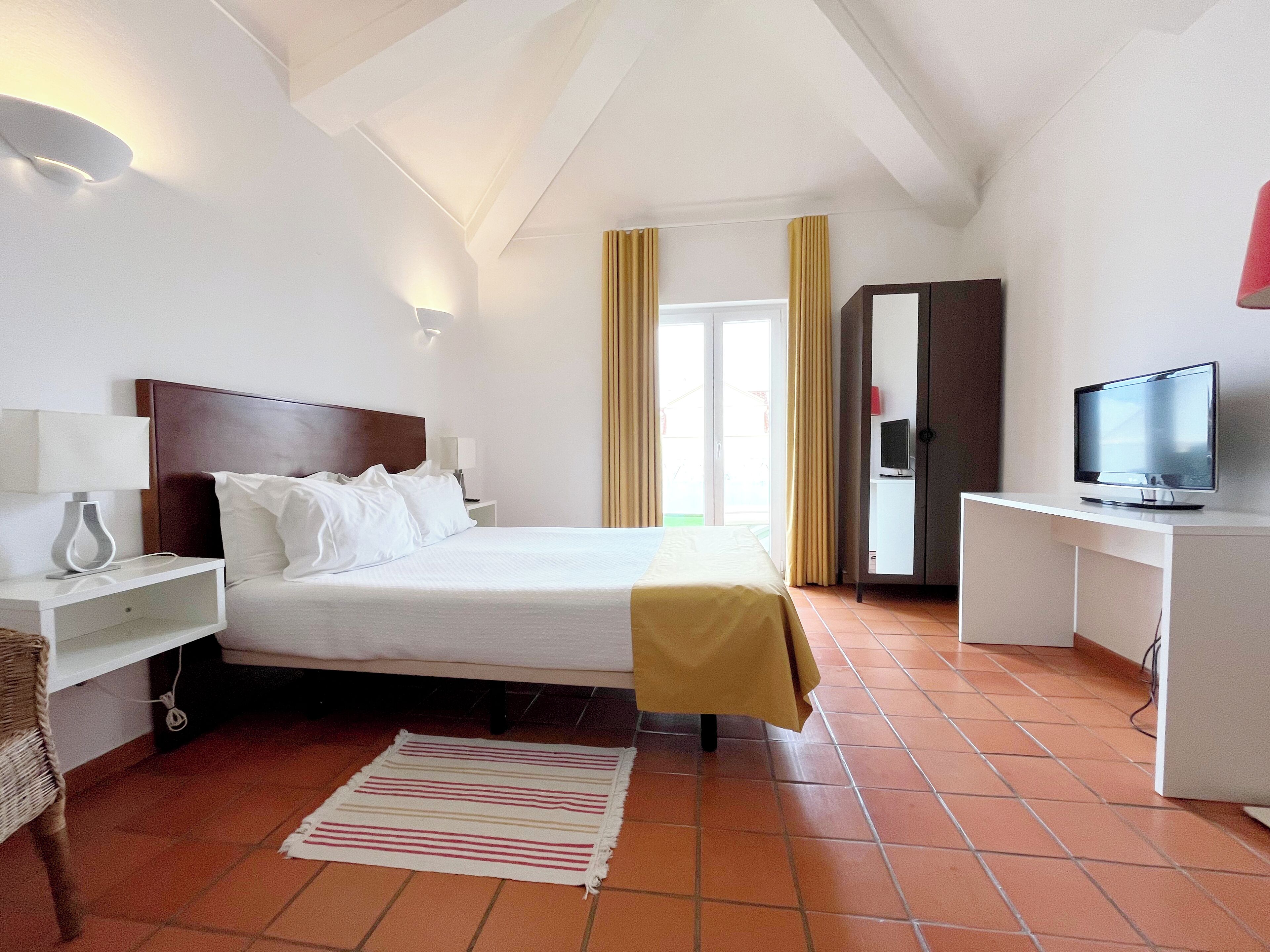 Une chambre d’hôtel comprenant un lit, des tables de chevet, une télévision, une armoire et une fenêtre avec des rideaux.