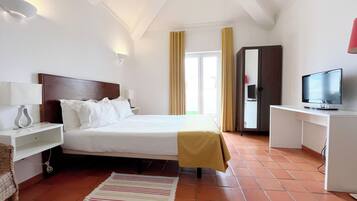 Une chambre d’hôtel comprenant un lit, des tables de chevet, une télévision, une armoire et une fenêtre avec des rideaux.