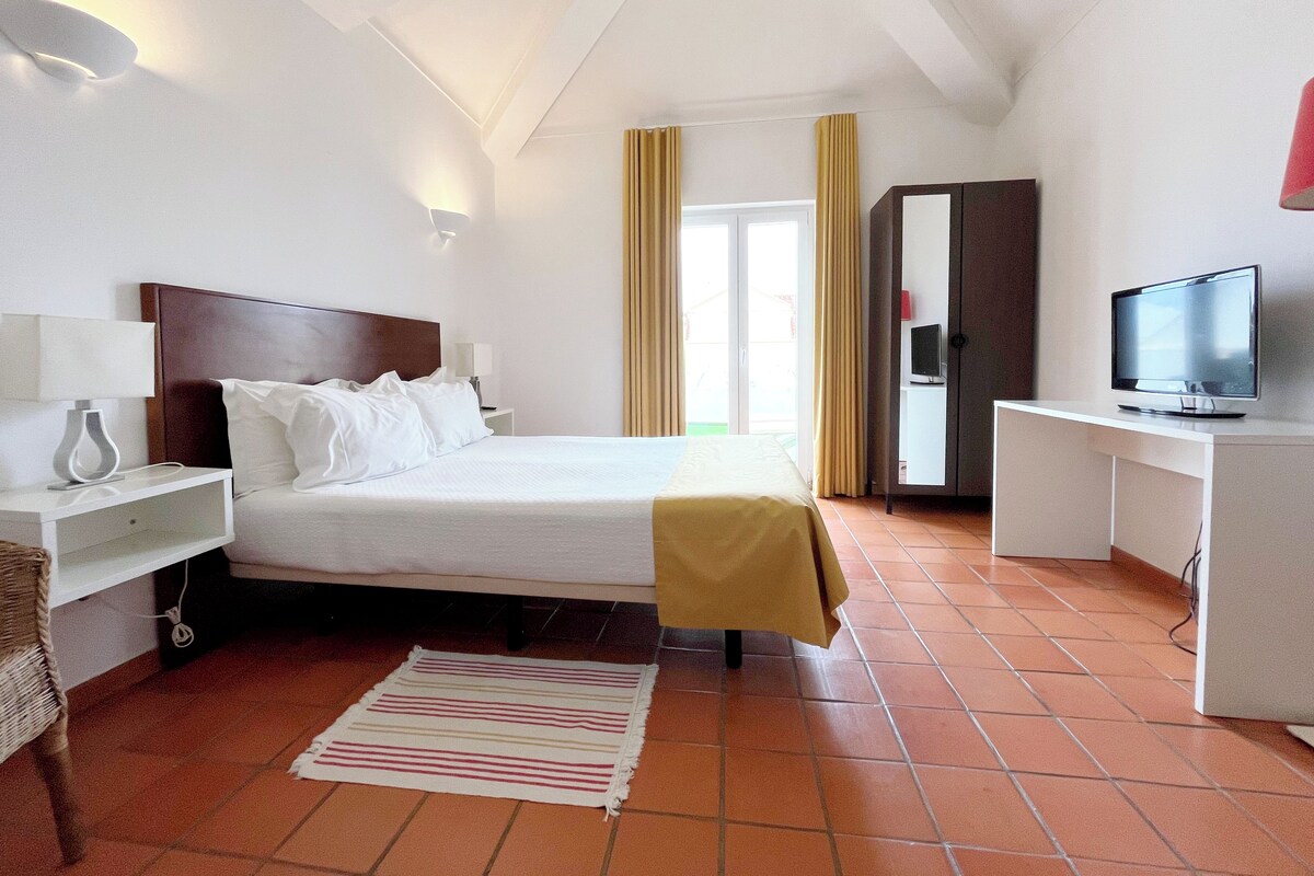 A hotel room with a bed, bedside tables, a TV, a wardrobe, and a window with curtains.