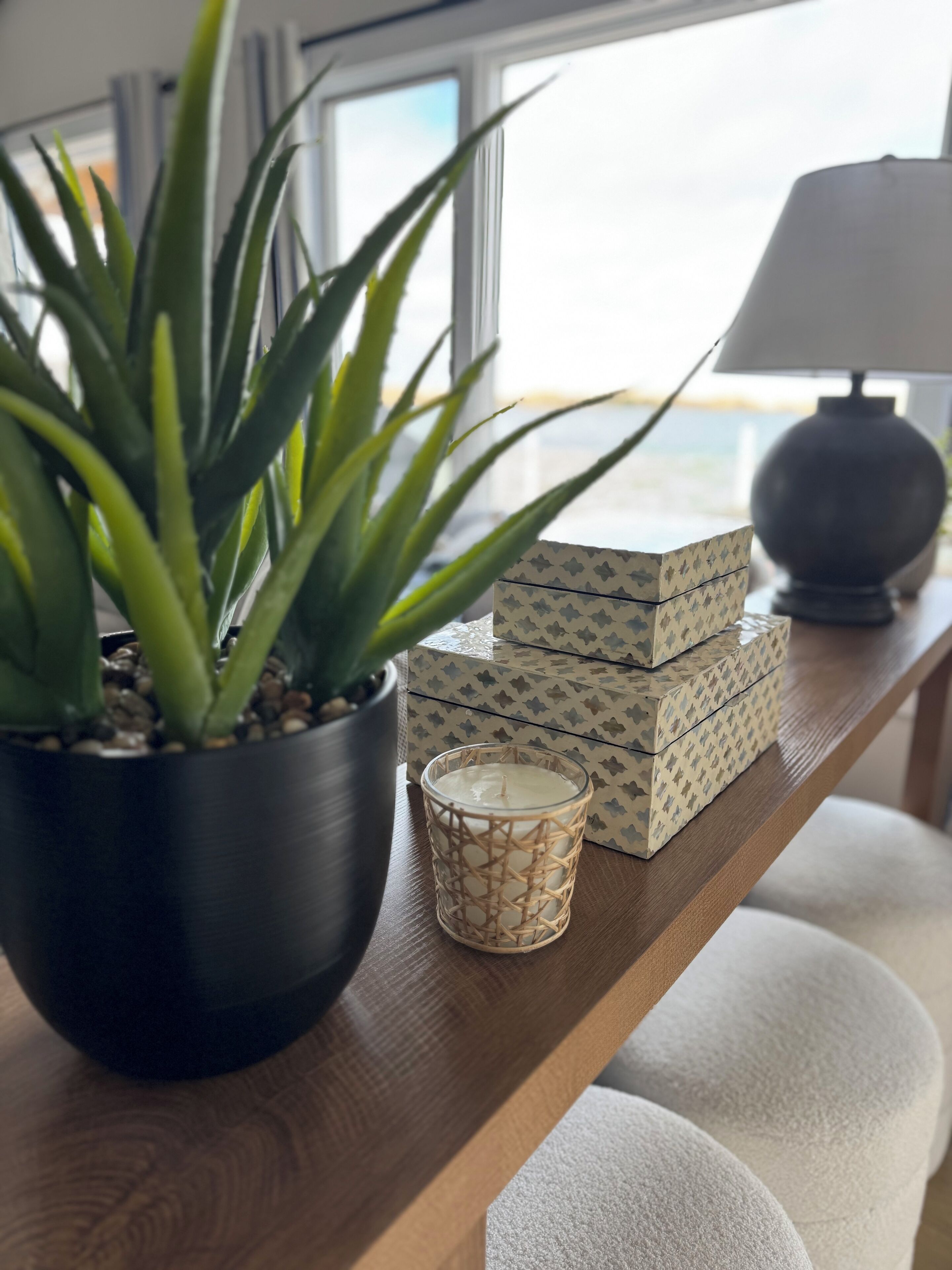 A potted plant, a candle, and patterned boxes on a wooden table.