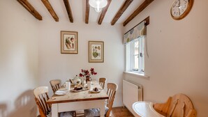 A dining room with a wooden table, chairs, and a baby rocker. There are two framed pictures on the wall, a window with a view, and a clock. - Swallow Cottages, No. 1 - UK46811 (Wickmere)