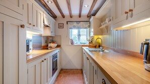 A narrow kitchen with wooden beams, white cabinets, and a wooden countertop. - Swallow Cottages, No. 1 - UK46811 (Wickmere)