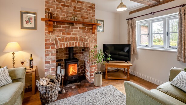 A cozy living room with a brick fireplace, a television, and comfortable seating. - Swallow Cottages, No. 1 - UK46811 (Wickmere)