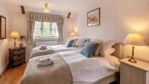 A cozy bedroom with two beds, a window with curtains, a bedside table with a lamp, and a framed picture on the wall. - Swallow Cottages, No. 1 - UK46811 (Wickmere)