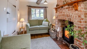 A cozy living room with a brick fireplace, a sofa, a window with curtains, and a small table with a lamp. - Swallow Cottages, No. 1 - UK46811 (Wickmere)