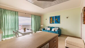 A room with a dining table, chairs, a sofa, and a view of the sea.
