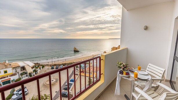 A balcony with a table set for breakfast overlooking a beach and the sea.