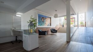 A spacious room with a desk, two chairs, a large painting, and a staircase leading to an outdoor area.