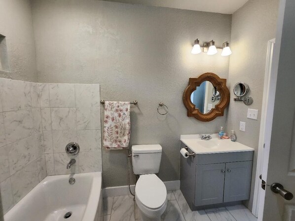 A bathroom with a bathtub, toilet, vanity, and a mirror.