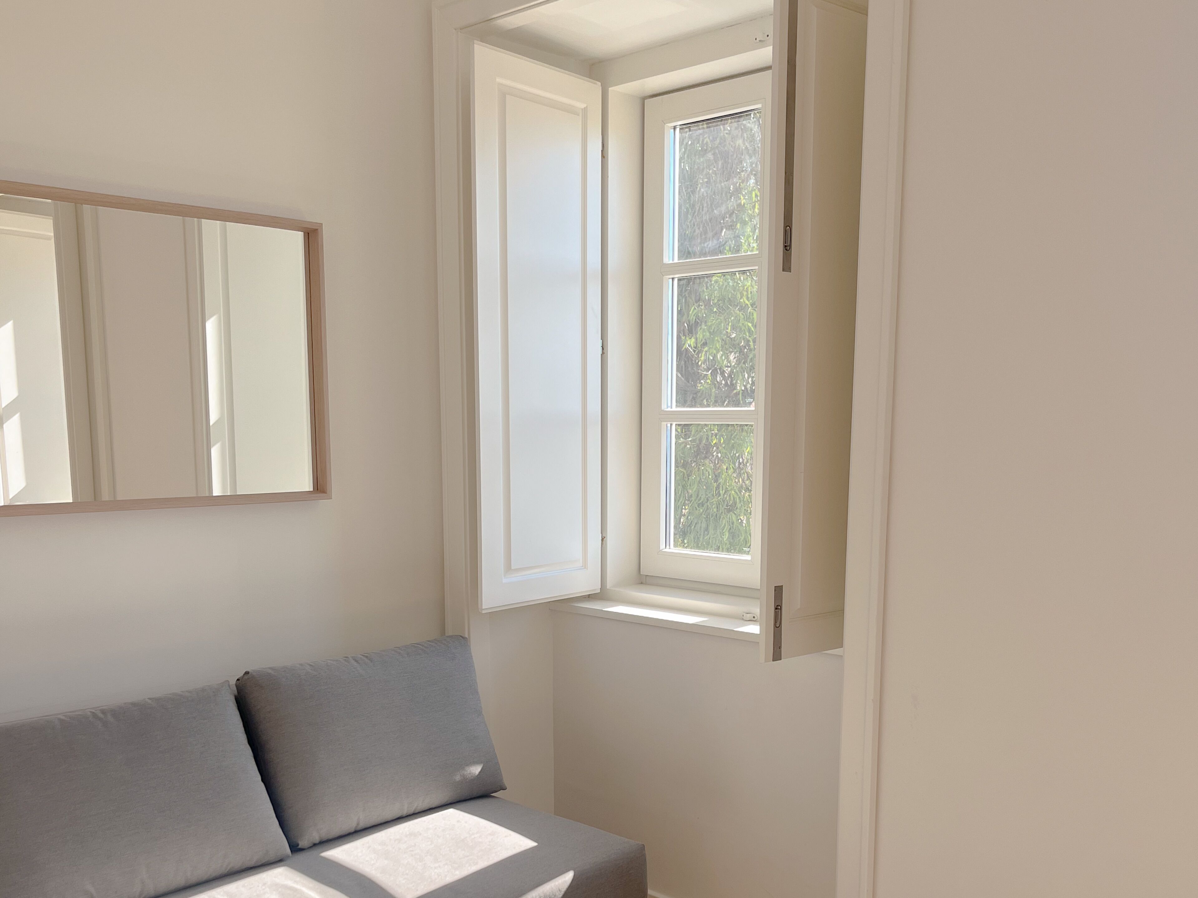 A room with a bed, a window, and a mirror on the wall.