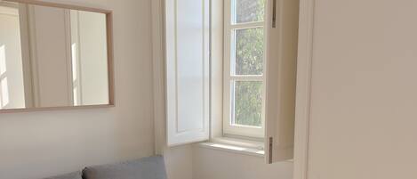 A room with a bed, a window, and a mirror on the wall.