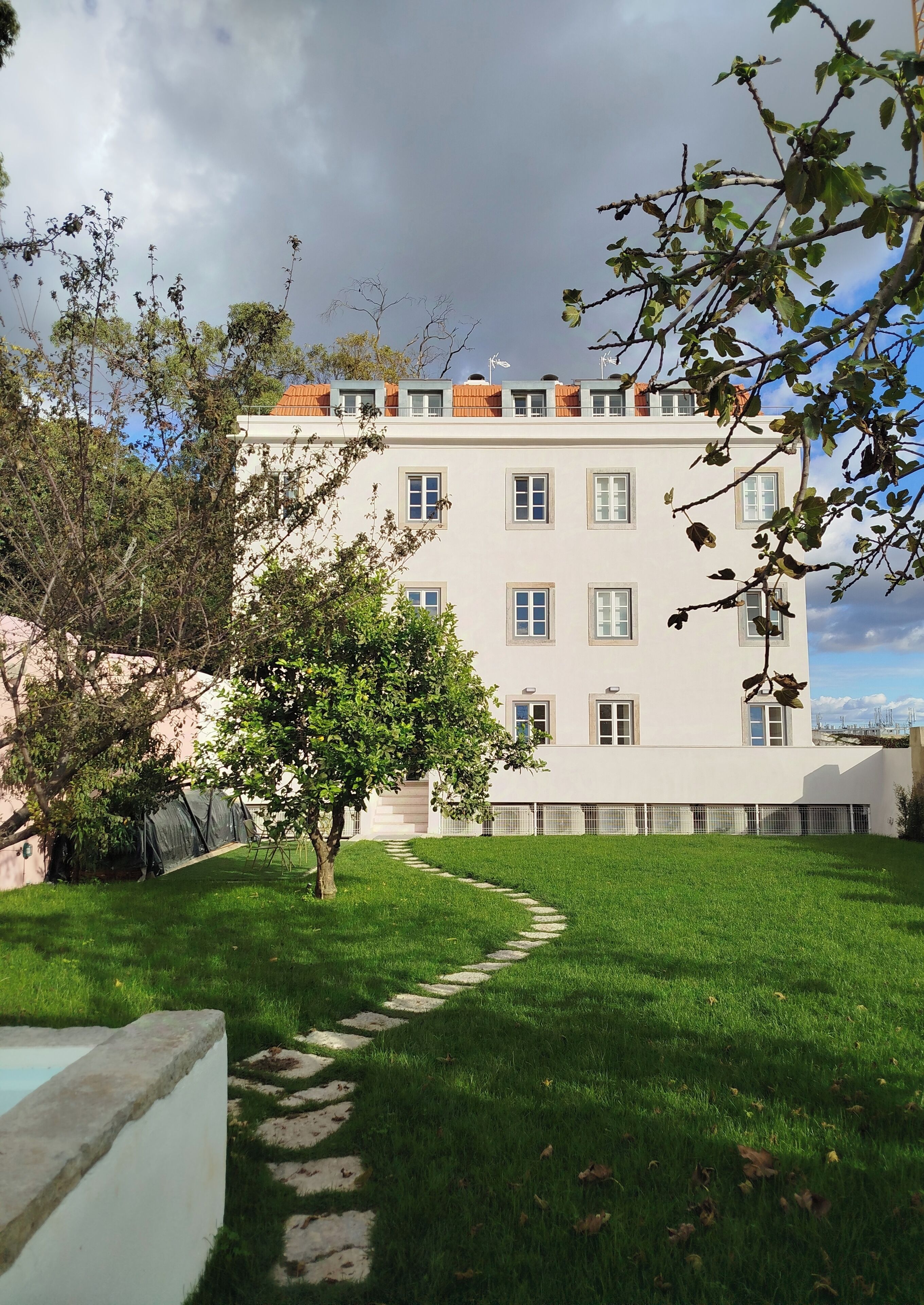 A multi-story building with a white facade, a rooftop terrace with orange tiles, and a clear sky.