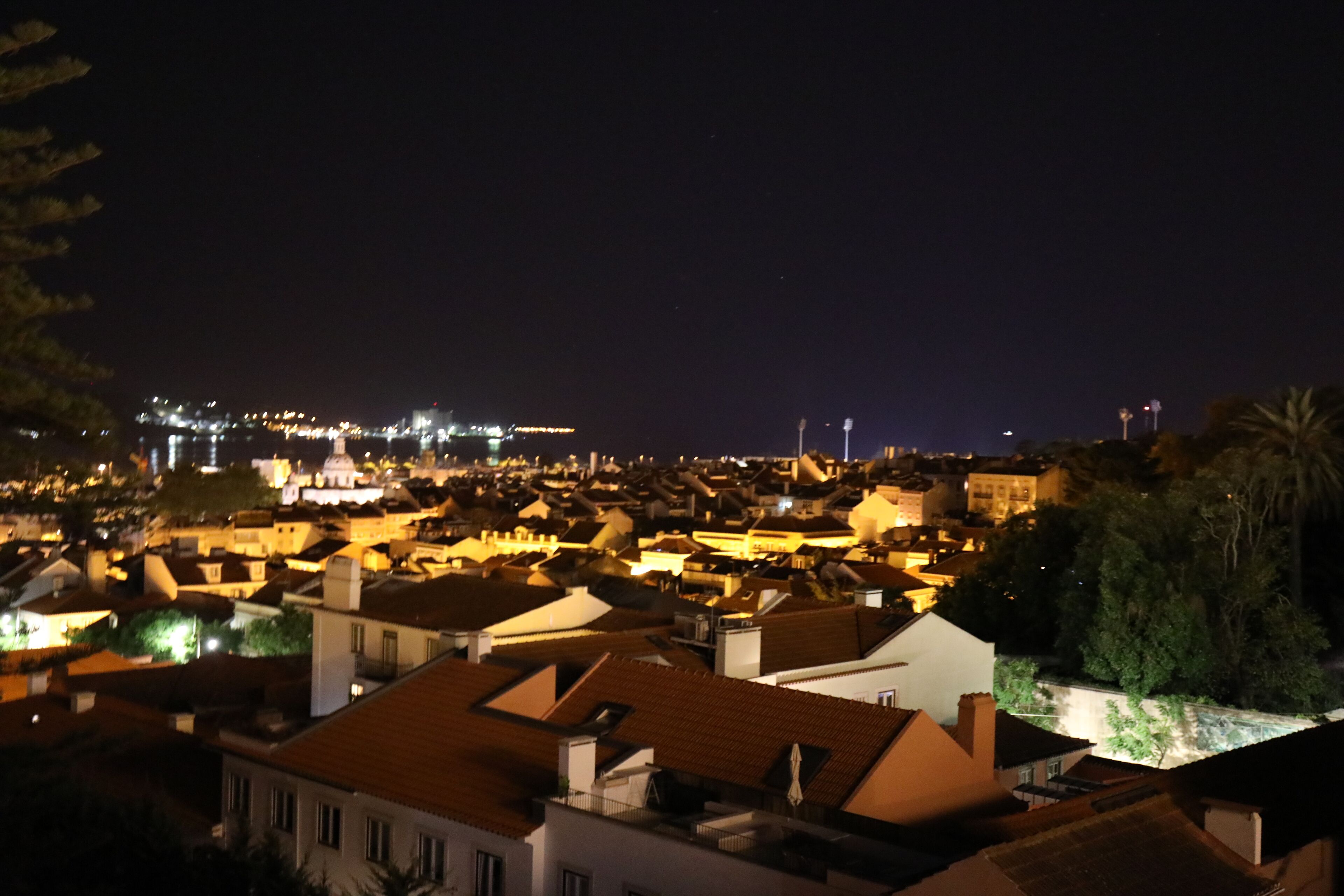 A nighttime view of a densely packed urban area with illuminated buildings and a river in the foreground.
