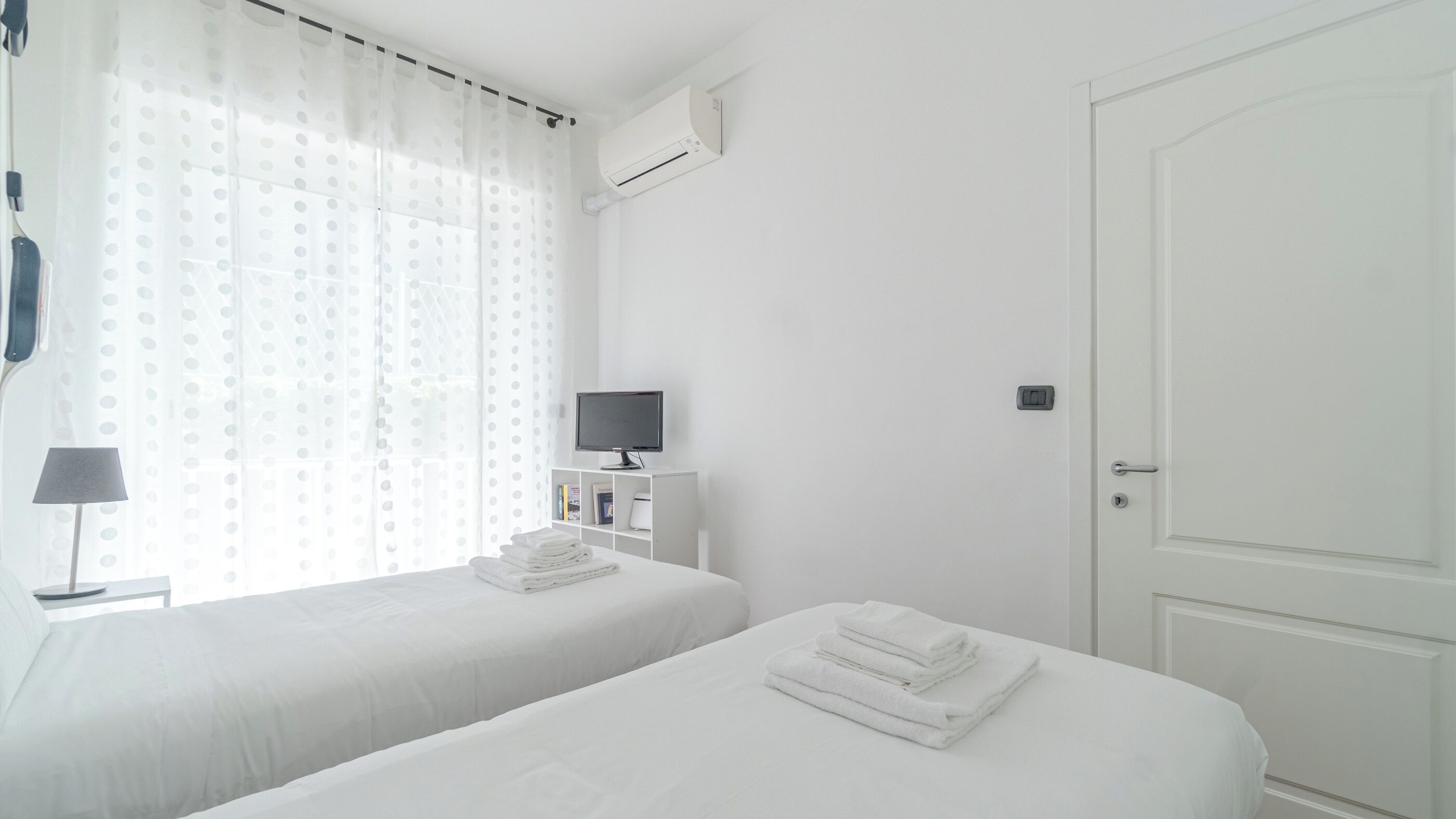 Habitación de hotel con dos camas, un televisor sobre un soporte, una lámpara y una puerta.