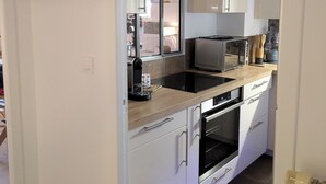 Une cuisine compacte avec des meubles blancs, un four à micro-ondes, un grille-pain et une machine à café.