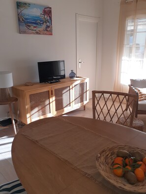 A living room with a television on a wooden cabinet, a dining table with a woven placemat, and a basket of fruit on the table. - Appartement a Bandol a 10 Minutes des Calanques (Bandol)