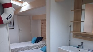 Une chambre avec deux lits, une salle de bain avec un lavabo et un miroir, et une lucarne au-dessus des lits.