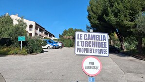Un panneau indiquant qu’il s’agit d’une propriété privée, nommée « Le Camelia L’Orchidée », un panneau d’interdiction d’accès, et une rue bordée de voitures garées, avec des bâtiments en arrière-plan.