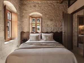 Een slaapkamer met een stenen muur, een houten bed en een raam met uitzicht op groen.