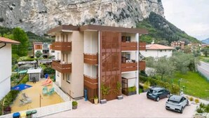 Un immeuble à plusieurs étages doté de balcons, d’une aire de jeux et d’une voiture garée devant.