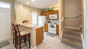 A compact kitchen with a refrigerator, microwave, stove, and wooden cabinets. - Disney Area Condo w/ 4 Pools & Arcade Fun (Kissimmee)