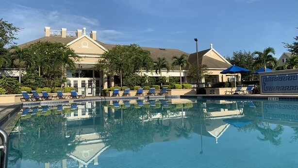 A swimming pool with lounge chairs and umbrellas, a building with a triangular roof, and palm trees. - Disney Area Condo w/ 4 Pools & Arcade Fun (Kissimmee)