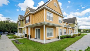 A two-story residential building with a gabled roof, a front porch, and a white picket fence. - Disney Area Condo w/ 4 Pools & Arcade Fun (Kissimmee)