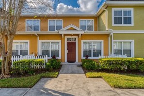 A two-story residential building with a front entrance, a picket fence, and a well-maintained lawn.