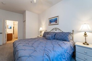 A bedroom with a bed, two bedside tables with lamps, a door leading to another room, and a painting on the wall.