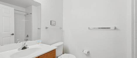 Un baño con lavamanos, tocador, espejo e inodoro blancos.