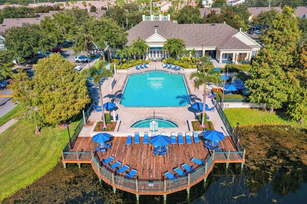 A resort with a central swimming pool, a wooden deck with lounge chairs, and a building with a white facade.
